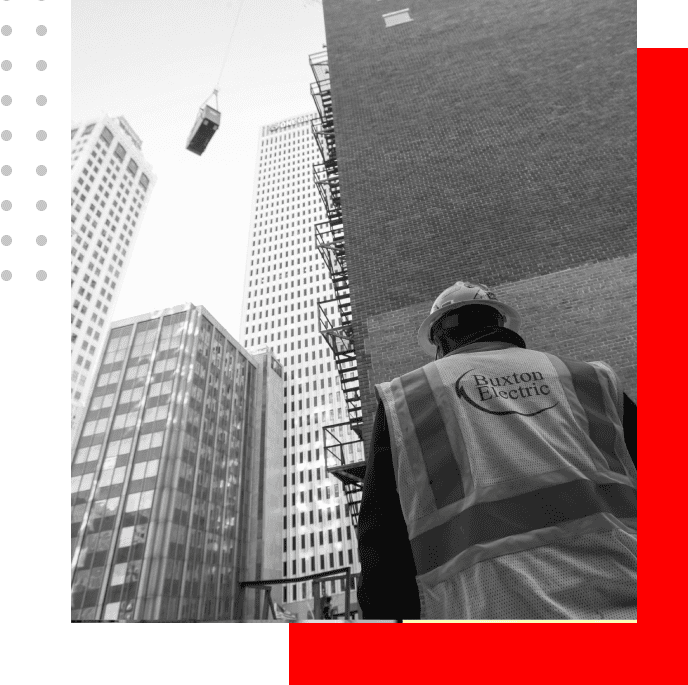 A man in safety gear looking up at tall buildings.